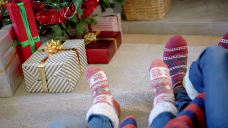 Moving-feet-of-family-in-warm-socks-by-christmas-tree-and-presents,-copy-space,-slow-motion