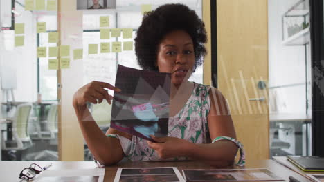 Animación-De-Gráficos,-Mapas-Y-Barras-De-Carga-Sobre-Una-Mujer-Afroamericana-Mostrando-Fotos-En-Videollamada