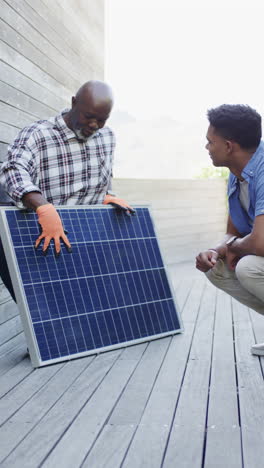 Vertical-video-of-african-american-father-explaining-solar-panel-to-son-outdoors,-slow-motion