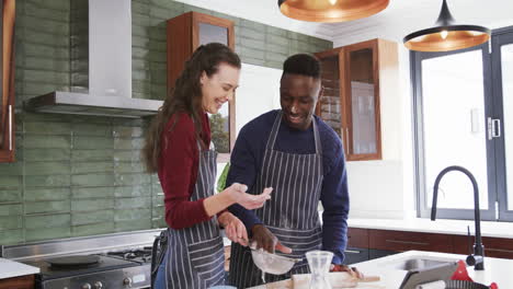 Happy-diverse-couple-standing-in-kitchen,talking,rolling-dough-and-getting-dirty,slow-motion