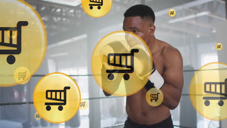 Animation-of-shopping-cart-icons-over-african-american-male-boxer-practicing-punches-in-ring