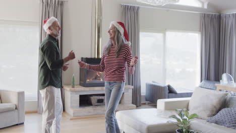Middle-aged-caucasian-couple-in-santa-hats-dancing-at-christmas-at-home,-slow-motion