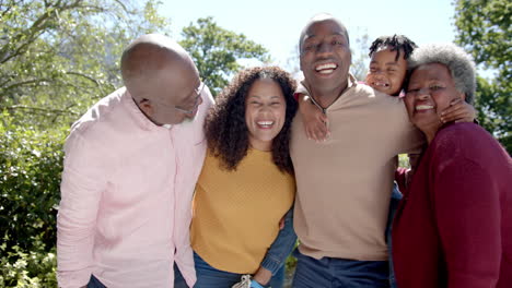 Portrait-of-happy-african-american-parents-and-son-and-grandparents-embracing-in-sunny-garden
