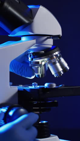 Vertical-video-of-close-up-of-laboratory-microscope-with-copy-space-on-blue-background