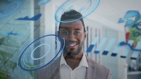 Animation-of-graphs,-globe-and-loading-circles-over-smiling-african-american-man-standing-in-office