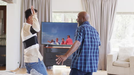 Excited-african-american-father-and-adult-son-cheering-at-sport-on-tv-and-high-fiving,-slow-motion