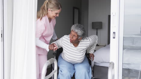 Smiling-caucasian-nurse-with-senior-african-american-woman-patient-in-wheelchair,-slow-motion