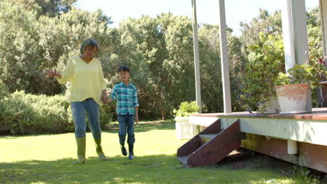 Happy-biracial-grandmother-and-grandson-walking-in-sunny-garden,-slow-motion,-copy-space
