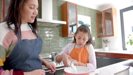 Happy-biracial-mother-and-daughter-preparing-dough-and-smiling-in-sunny-kitchen