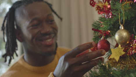 Hombre-Afroamericano-Sonriente-Con-Rastas-Decorando-El-árbol-De-Navidad,-Cámara-Lenta