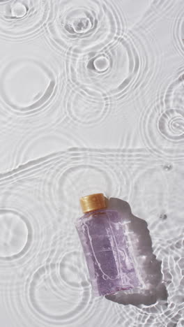Vertical-video-of-beauty-product-bottle-in-water-with-copy-space-on-white-background