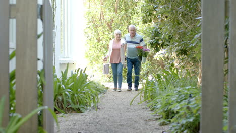 Senior-caucasian-couple-holding-flowers-and-walking-in-sunny-garden,-slow-motion