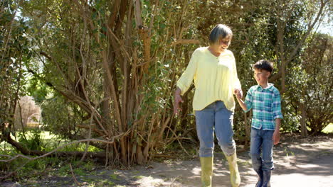 Happy-biracial-grandmother-and-grandson-walking-in-sunny-garden,-slow-motion