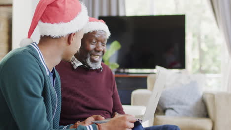 Glücklicher-Afroamerikanischer-Vater-Und-Erwachsener-Sohn-In-Weihnachtsmützen-Mit-Laptop-Videoanruf,-Zeitlupe
