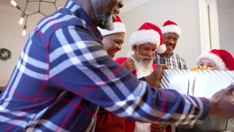 Happy-diverse-senior-friends-in-santa-outfit-and-christmas-hats-exchanging-gift-at-home,-slow-motion