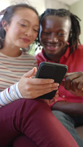 Vertical-video-of-happy-diverse-couple-using-smartphone-in-sunny-living-room,-slow-motion