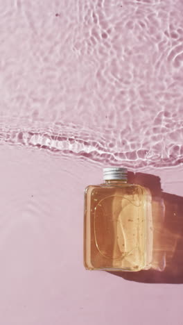 Vertikales-Video-Einer-Kosmetikflasche-Im-Wasser-Mit-Kopierraum-Auf-Rosa-Hintergrund