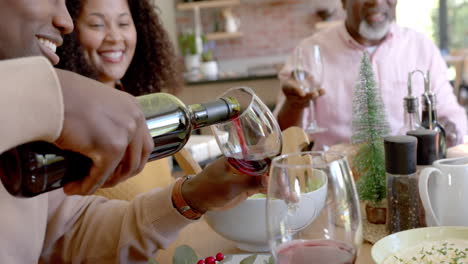 Happy-african-american-husband-pouring-wine-for-wife-and-senior-father-at-christmas-dinner-table