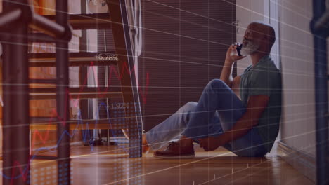 Animation-of-graphs,-numbers,-senior-african-american-man-sitting-on-floor-and-talking-on-cellphone