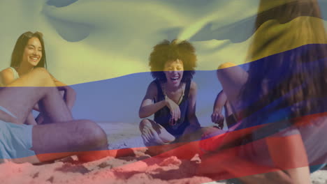 Animation-of-flag-of-colombia-waving-over-diverse-friends-enjoying-conversation-at-beach