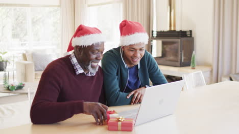 Happy-african-american-father-and-adult-son-in-christmas-hats-having-laptop-video-call,-slow-motion
