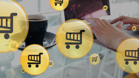 Animation-of-shopping-cart-icons,-coffee-cup,-cropped-hands-of-caucasian-woman-working-on-laptop
