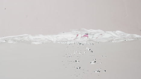 Video-of-beauty-product-bottle-falling-into-water-with-copy-space-on-white-background