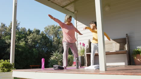 Ältere-Großmutter-Mit-Gemischter-Abstammung-Und-Enkel-Machen-Yoga-Und-Stretching-Auf-Der-Terrasse-Zu-Hause,-Zeitlupe