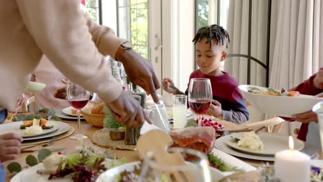 African-american-father-carving-meat-at-multi-generation-family-christmas-dinner-table