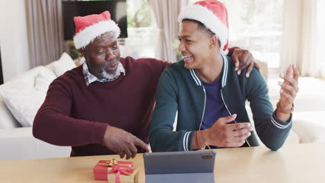 Happy-african-american-father-and-adult-son-in-christmas-hats-having-tablet-video-call,-slow-motion