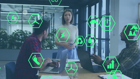 Animation-of-icon-in-hexagons-over-diverse-woman-explaining-strategy-to-coworkers-in-office