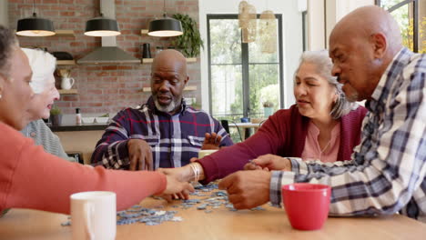 Happy-diverse-senior-female-and-male-friends-talking-and-doing-jigsaw-puzzle-in-kitchen,-slow-motion
