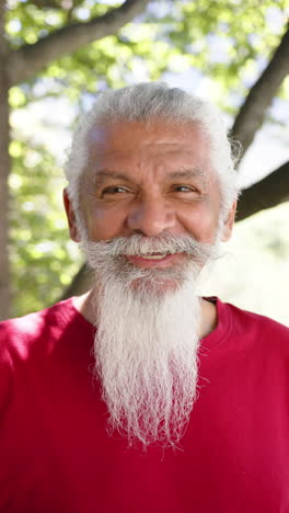 Vertical-video-portrait-of-senior-biracial-man-with-white-beard-smiling-in-sunny-nature,-slow-motion