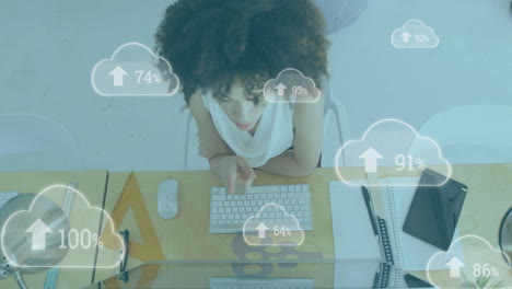 Animation-of-arrow,-changing-numbers-in-clouds-over-biracial-woman-working-on-computer