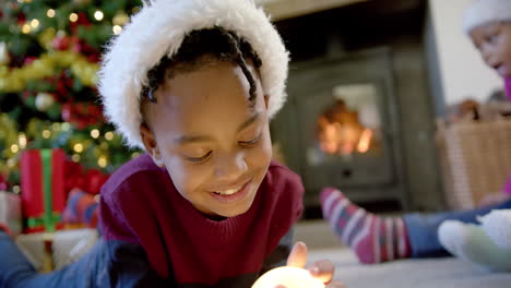 Glücklicher-Afroamerikanischer-Sohn-In-Weihnachtsmütze-Mit-Schneekugel,-Familie-Im-Hintergrund,-Zeitlupe