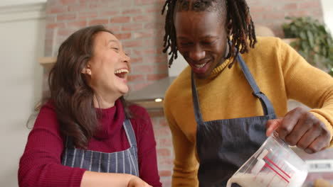 Happy-diverse-couple-in-aprons-having-fun-baking-in-kitchen,-slow-motion