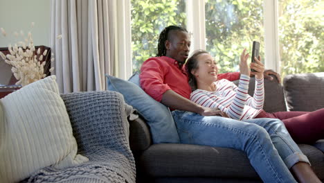 Happy-diverse-couple-relaxing-on-couch-using-tablet-in-living-room,-copy-space,-slow-motion