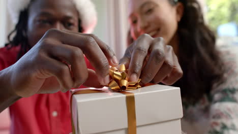 Happy-diverse-couple-sticking-bow-on-christmas-gift-at-home,-slow-motion