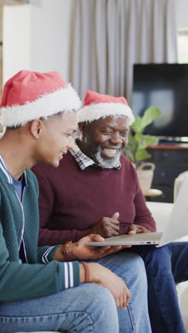Vertical-video-of-happy-african-american-father-and-son-in-christmas-hats-using-tablet,-slow-motion