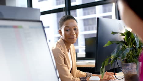 Portrait-of-smiling-african-american-businesswoman-by-computer-in-office,-slow-motion,-copy-space