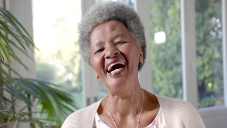 Portrait-of-happy-senior-african-american-woman-laughing-in-sunny-living-room,-slow-motion