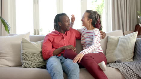 Portrait-of-happy-diverse-couple-sitting-on-couch-talking-in-sunny-living-room,-slow-motion