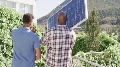 Afroamerikanischer-Vater-Hält-Solarpanel-Und-Spricht-Mit-Erwachsenem-Sohn-Im-Sonnigen-Garten,-Zeitlupe