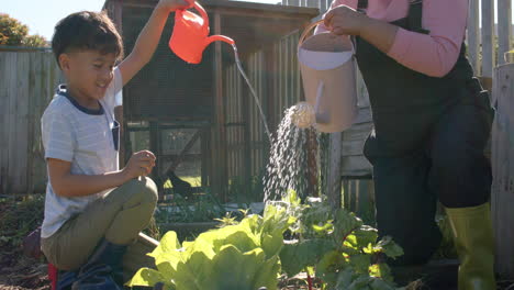 Senior-biracial-grandmother-and-grandson-watering-plants-in-sunny-garden,-slow-motion