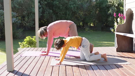 Senior-biracial-grandmother-and-grandson-doing-yoga,-stretching-on-terrace,-slow-motion