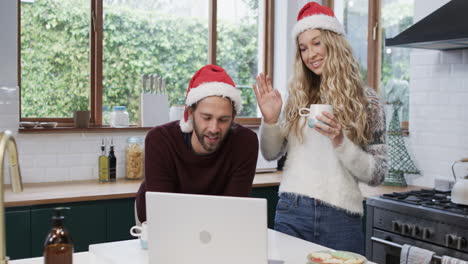 Vielfältiges-Paar-Mit-Weihnachtsmützen,-Das-Einen-Laptop-Für-Einen-Weihnachtsvideoanruf-In-Zeitlupe-Verwendet