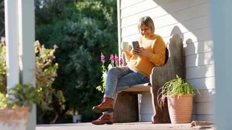 Glückliche-ältere-Frau-Mit-Gemischter-Abstammung,-Die-Ihr-Smartphone-Benutzt-Und-Auf-Der-Terrasse-Kaffee-Trinkt,-Zeitlupe,-Kopierraum