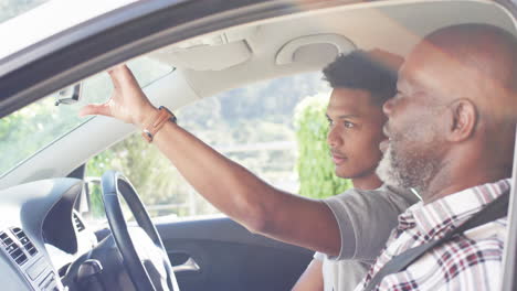 Happy-african-american-father-instructing-son-about-mirror-in-car-before-driving-lesson,-slow-motion