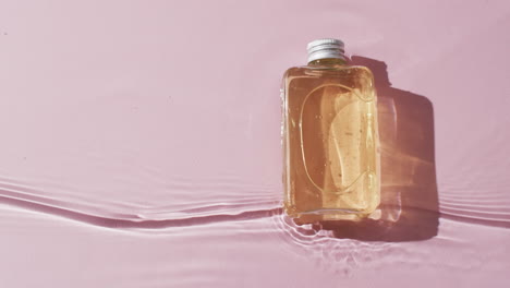 Video-of-beauty-product-bottle-in-water-with-copy-space-on-pink-background