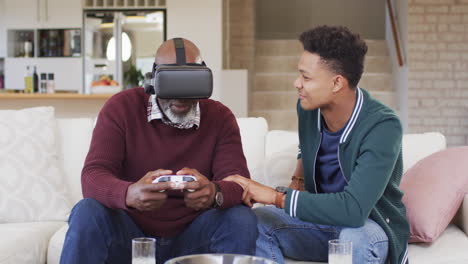 Glücklicher-Afroamerikanischer-Vater-Mit-VR-Headset-Und-Gamepad-Mit-Erwachsenem-Sohn-Zu-Hause,-Zeitlupe